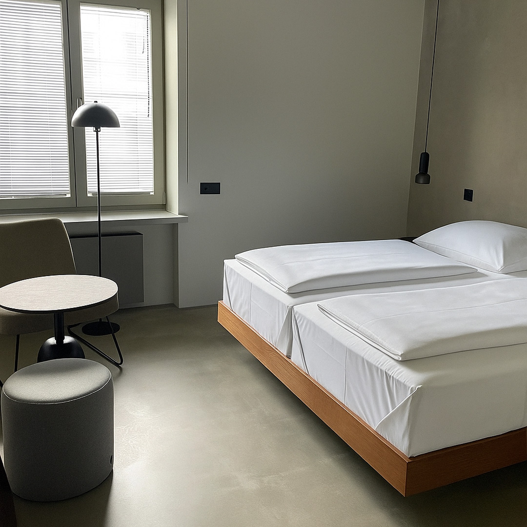 Blick auf großes Doppelbett im modern eingerichteten Doppelzimmer Standard – zwei Kopfkissen, schlichtes Kopfteil und angenehme Beleuchtung